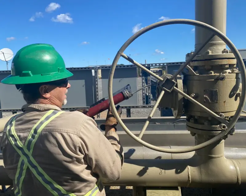 ShalePro field technician in a hard hat, safety glasses, and flame-resistant PPE servicing a valve
